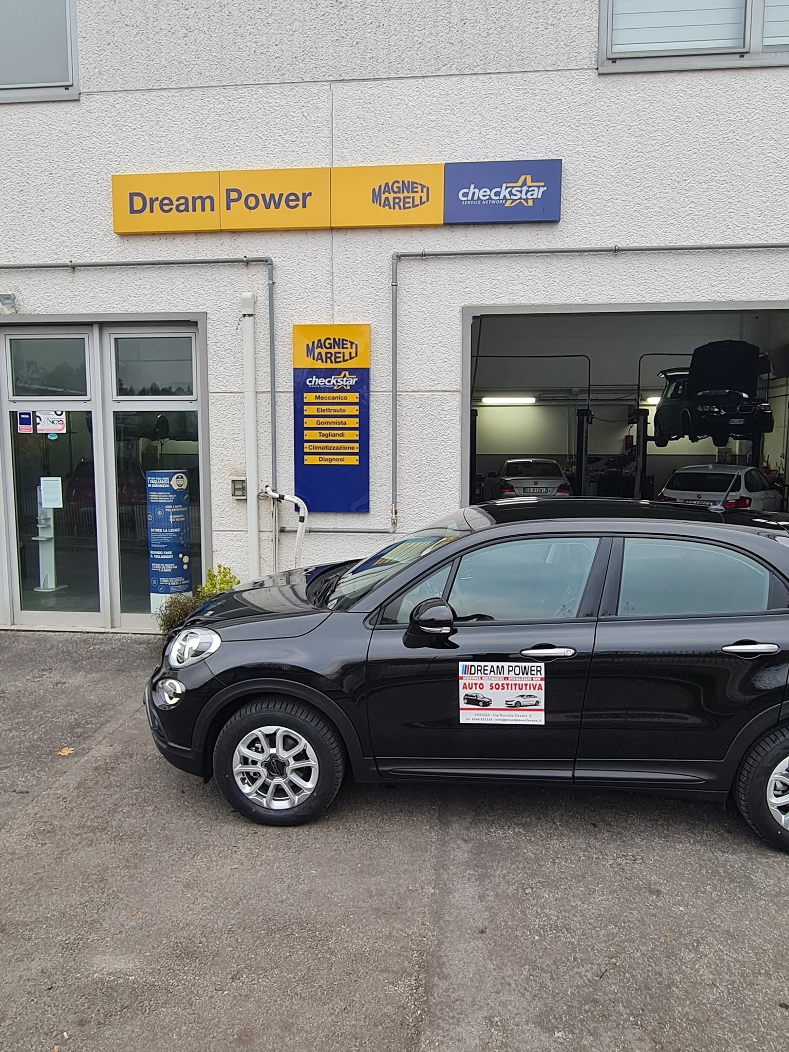 Dream Power - Esterno officina con auto sostitutiva e insegna Magneti Marelli Checkstar
